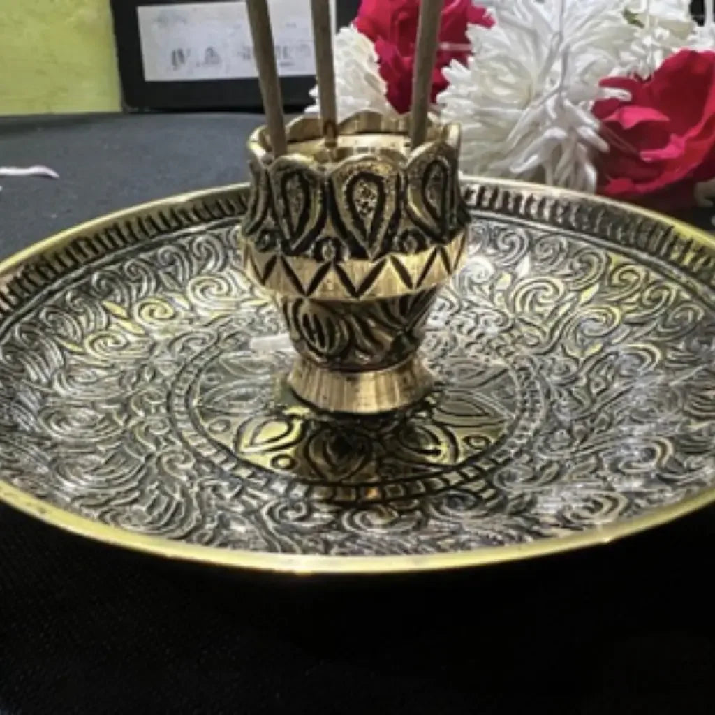 Decorative brass holder on a patterned tray with flowers in the background
