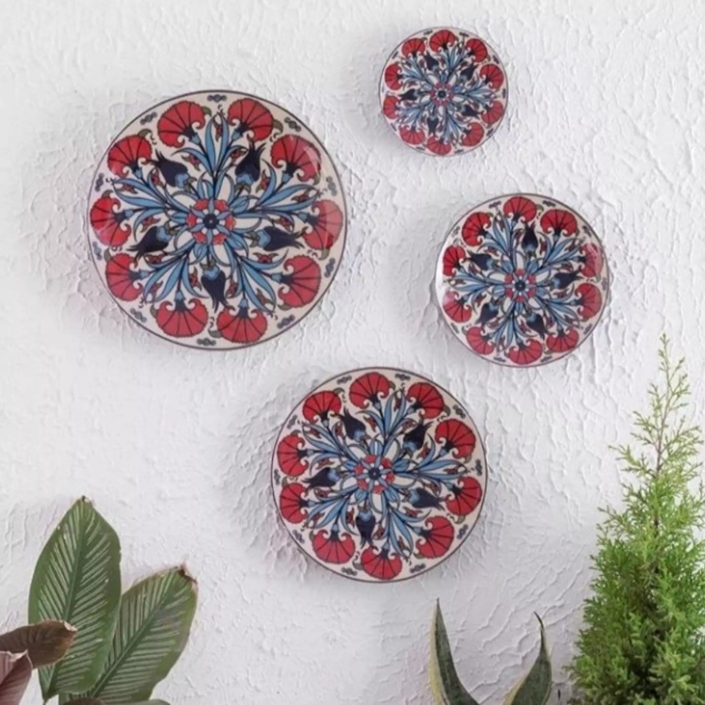 Set of four decorative plates with red and blue floral patterns on a white wall.