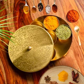 Decorative brass spice box with spices placed on a wooden table.