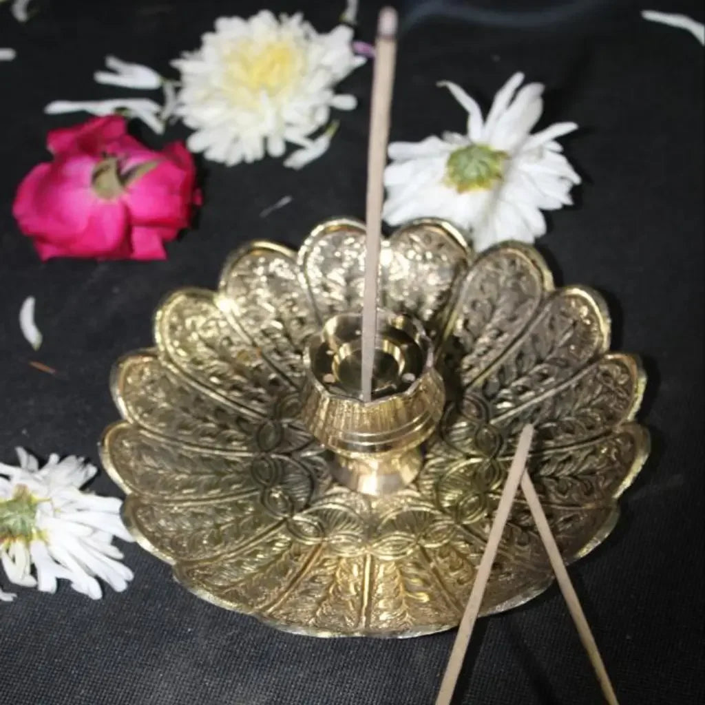 Decorative gold incense burner with incense sticks on a black background with flowers.