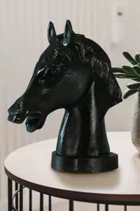 Black horse head sculpture on a white surface with a plant in the background