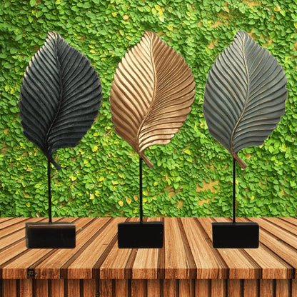 Three leaf-shaped decorative items on stands against a green leafy background