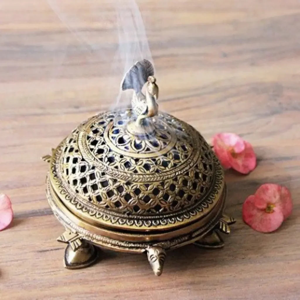 Decorative brass incense burner with intricate designs on a wooden surface with pink flowers.