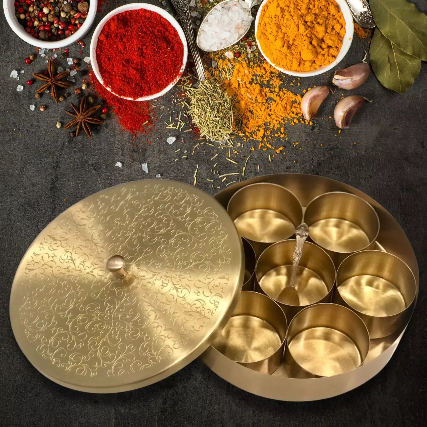 Gold spice box with compartments on a dark surface with spices around