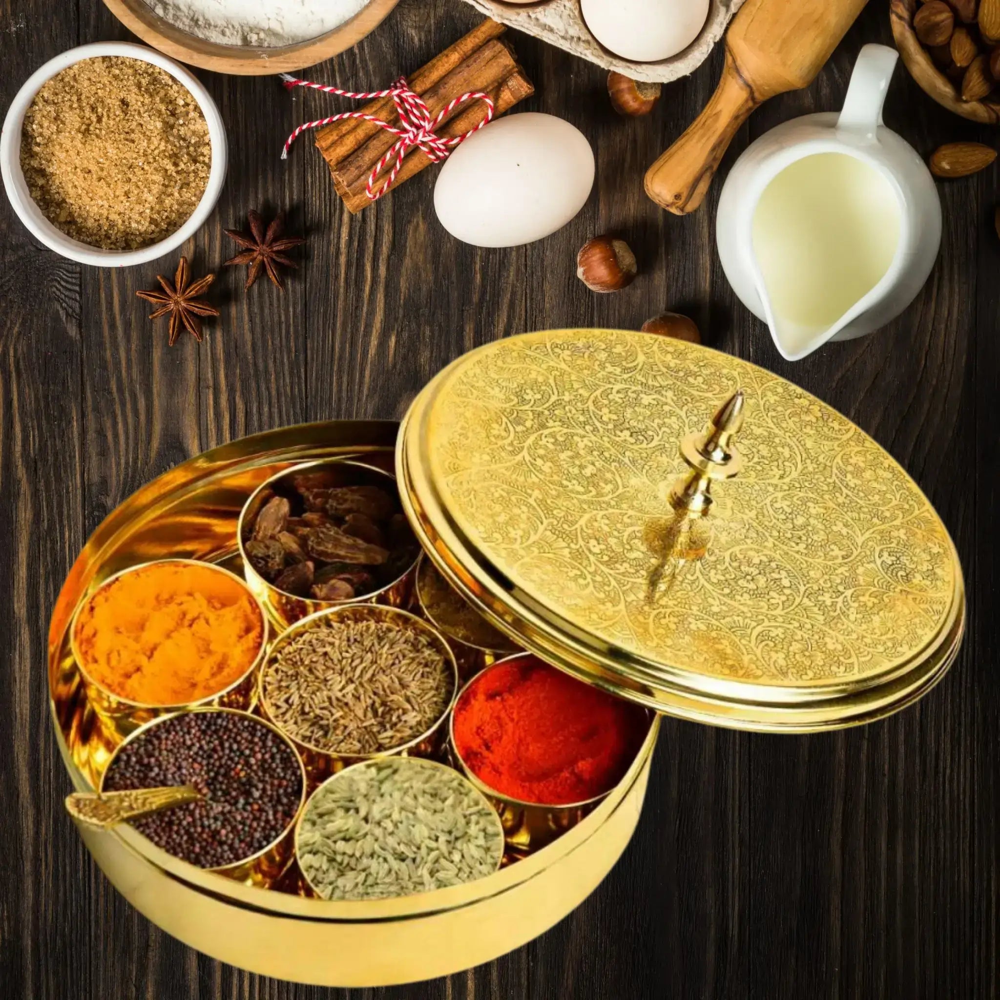 Gold spice box with colorful spices on a wooden surface with ingredients like eggs and milk.
